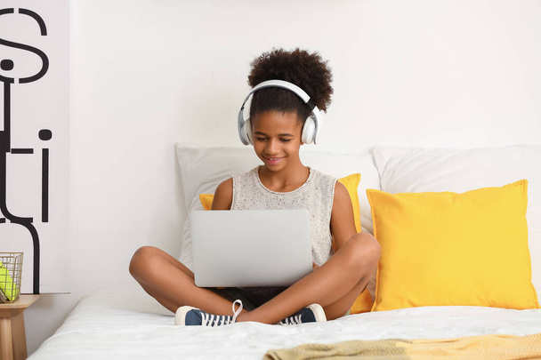 Teenage African-American girl with headphones and laptop at home - Foto, immagini