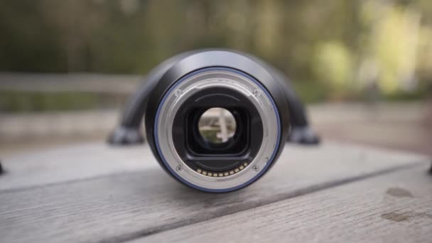 Details of the camera lens with opened aperture, close up view. Action. Camera lens on a wooden rotating children carousel outdoors on the background of green trees. - Footage, Video