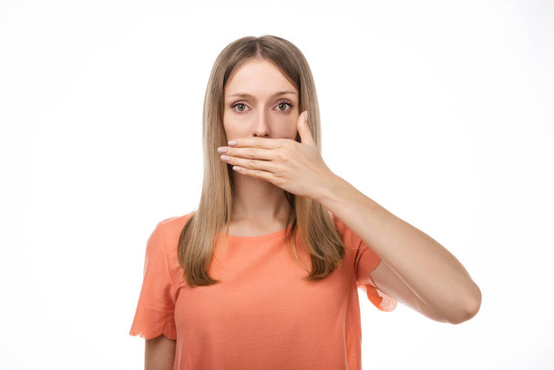 Frustrated blond girl in casual clothes is covering mouth with hand not willing to disclose something important. Keep a secret. Studio shot, white background - Fotoğraf, Görsel