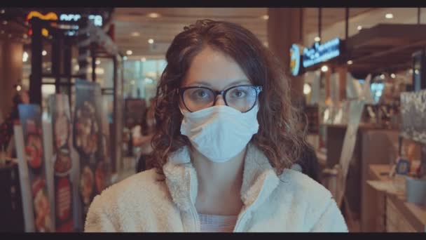 woman wearing face mask and looking at the camera in shopping mall. woman in white sweater with face mask in mall - Filmmaterial, Video
