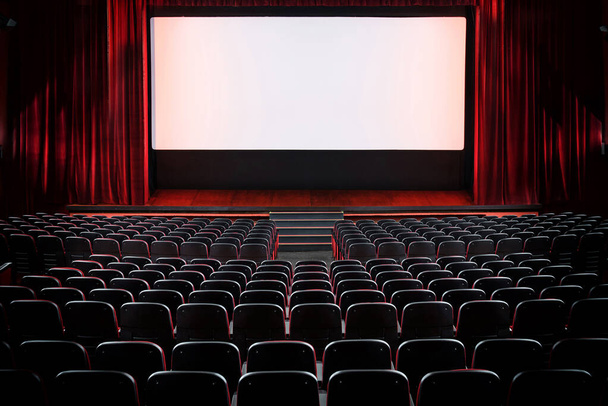 Auditorium prázdného kina a jeviště s rozepnutými červenými sametovými závěsy ze zadní části řady sedadel se světly na plátně - Fotografie, Obrázek