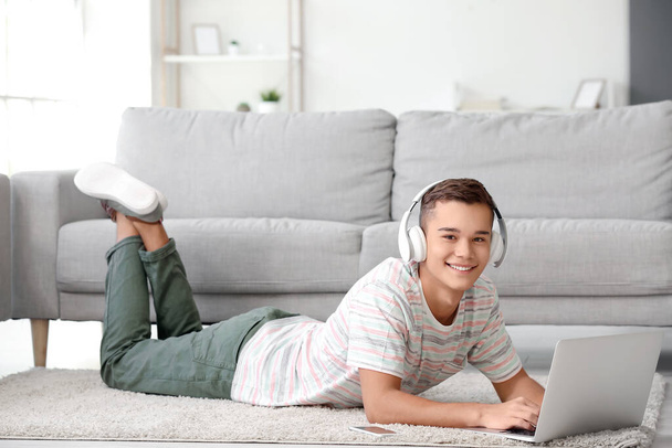 Tienerjongen met hoofdtelefoon en laptop thuis - Foto, afbeelding