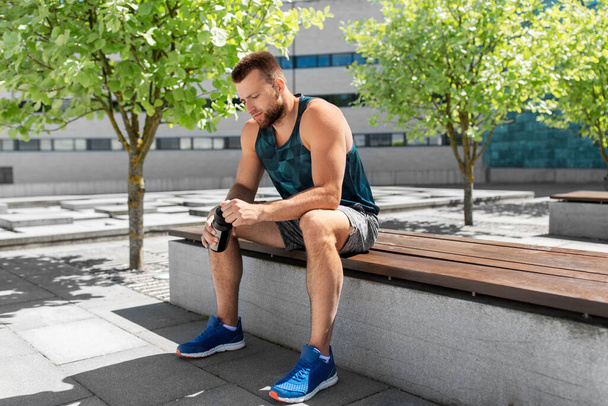tired sportsman with bottle sitting on city bench - Photo, image