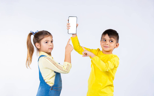 Preschool children on a white background point with a forefinger at the smartphone screen and look to the side. - Foto, afbeelding