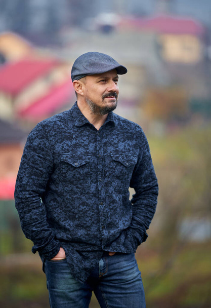 Closeup of a farmer in blue jeans, shirt and cap with village in the background - Zdjęcie, obraz