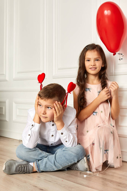 little child boy holding two red hearts on stick and girl with red heart shaped balloons - Фото, изображение
