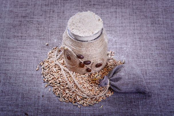 Vintage jar of white flour stands in the middle of a pile of grain and on a rag background - Photo, image
