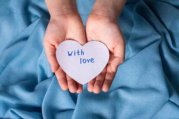 las manos de los niños sostienen un corazón de papel blanco con la inscripción con amor - Foto, imagen