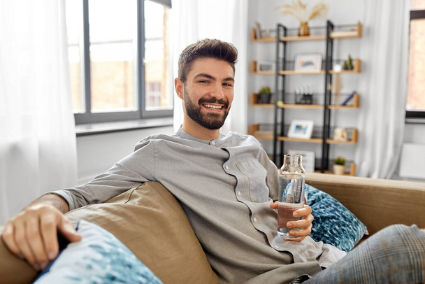 happy man drinking water from glass bottle at home - Foto, Imagem
