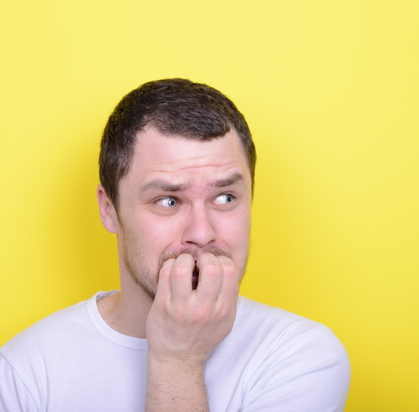 Portrait of man biting nails against yellow background - Foto, Bild