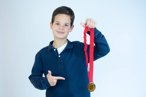 Mladý chlapec ukazuje svou zlatou medaili na bílém pozadí. - Fotografie, Obrázek
