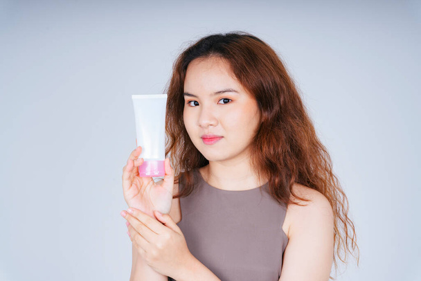 Портрет молодої азіатської кучерявої зачіски жінки, що тримає пляшку для лосьйону зі шкіри ізольовано на білому тлі
. - Фото, зображення
