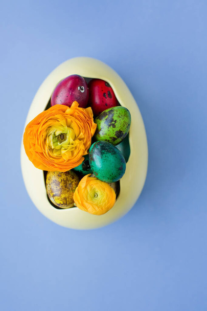Easter eggs and orange flowers in the yellow bowl on a blue background. Easter colorful concept - Fotoğraf, Görsel