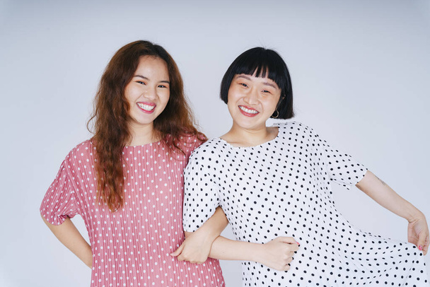Portrét dvou mladých asijských žen v bílém a růžovém palkadotu tančící drží paže pohromadě. - Fotografie, Obrázek