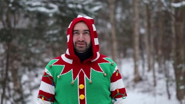 ritratto di un giovane che indossa un maglione natalizio e sorride alla telecamera, in mezzo alla foresta. - Filmati, video
