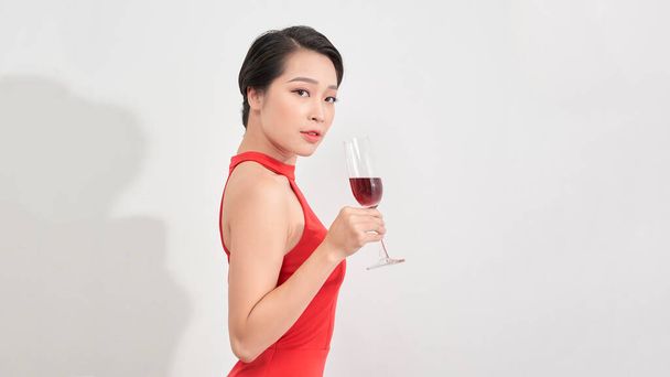 Young celebrating woman red dress. Beautiful model portrait isolated over studio background hold wine glass. - Photo, Image