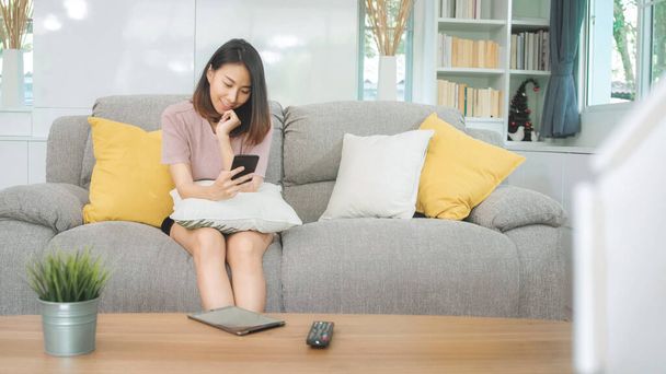 Giovane donna asiatica che utilizza smartphone controllare i social media sentirsi felici sorridendo mentre sdraiato sul divano quando rilassarsi in soggiorno a casa. Stile di vita donne latine ed etniche ispaniche al concetto di casa. - Foto, immagini