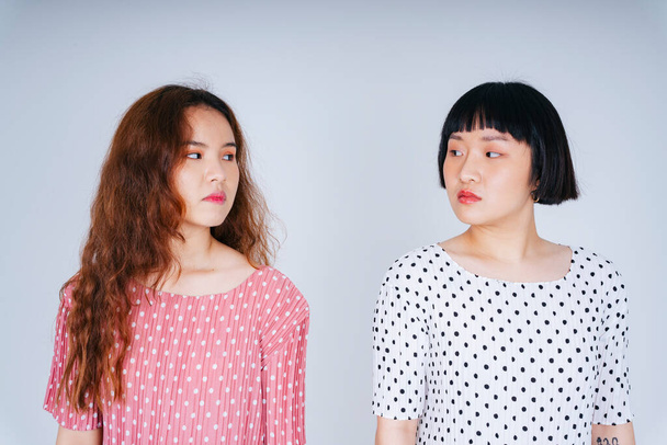 Portret dwóch młodych azjatyckich kobiet w różowej i białej sukience palkadot patrzących na siebie. - Zdjęcie, obraz