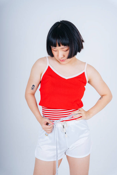 Portrait of young asian short bob hairstyle wearing red shirt using measure tape on her waist. - Foto, Imagem