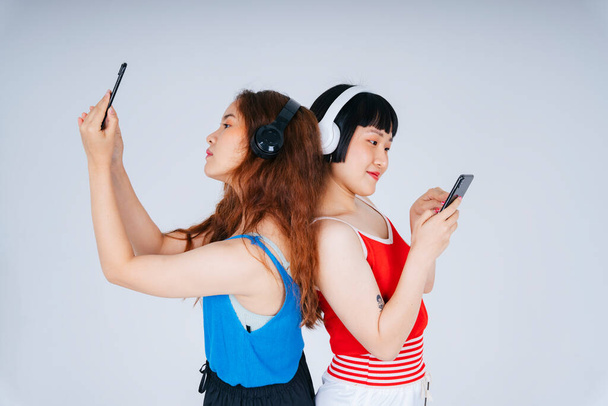 Portrait of two young asian women listen to music and playing mobile game isolate on white background. - Foto, imagen