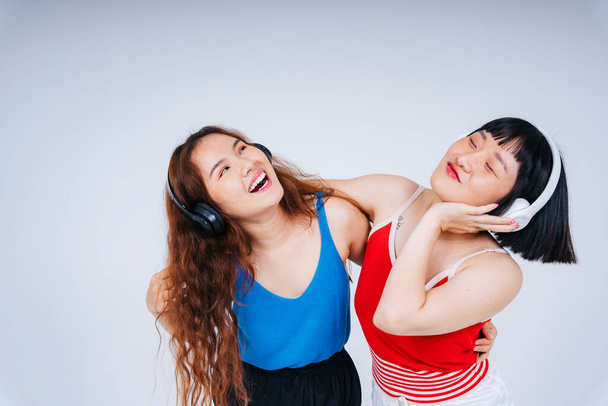 二人の若いアジアの女性の肖像は、白の背景に隔離された音楽とダンスを聴くのを楽しむ. - 写真・画像