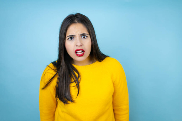 Young beautiful woman wearing yellow sweater over isolated blue background afraid and shocked with surprise and amazed expression, fear and excited face. - Photo, Image