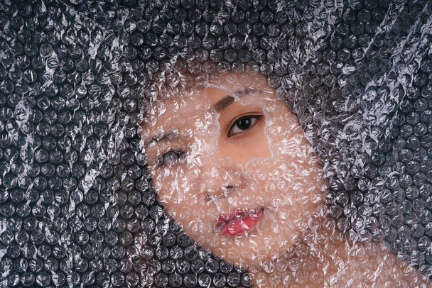 asiatique thai femme derrière plastique envelopper avec oeil sur un trou. Gros plan portrait. - Photo, image
