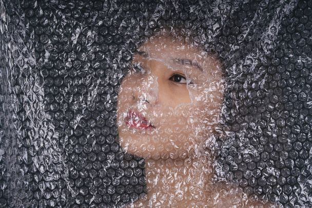 Mujer tailandesa asiática detrás de una envoltura de plástico con ojo en un agujero. Primer plano retrato. - Foto, imagen