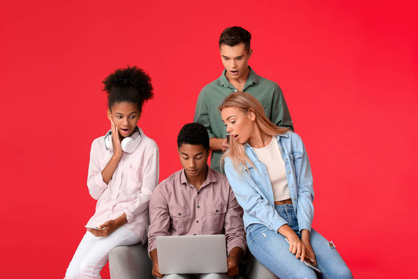 Surprised teenagers with modern laptop on color background - Photo, Image