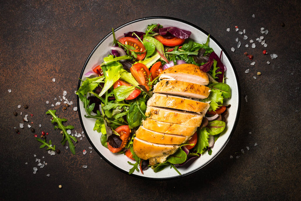 Green salad with baked chicken breast at kitchen table. - Photo, Image