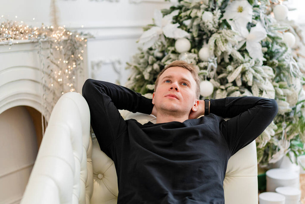 Gelukkige man met nieuwjaarscadeaus zittend op tapijt op kerstachtergrond. Vrolijk wit mannelijk model met Kerstmis in de studio. - Foto, afbeelding