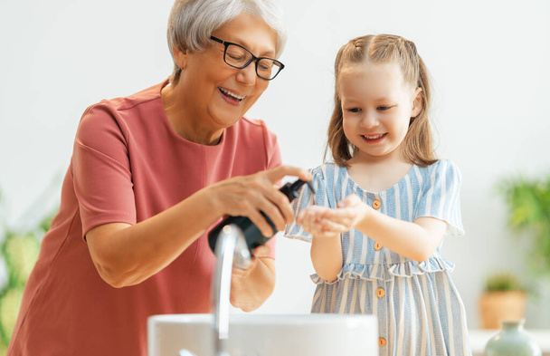 A cute little girl and her grandmother are washing their hands. Protection against infections and viruses.   - Фото, изображение