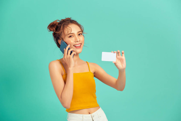 feliz jovem asiático mulher usando telefone e segurando cartão de crédito isolado sobre luz verde fundo. - Foto, Imagem