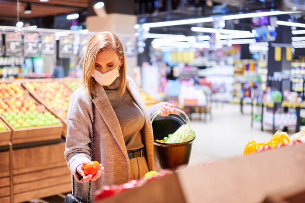 Женщина в медицинских масках делает покупки в продуктовом магазине во время вирусной пандемии - Фото, изображение