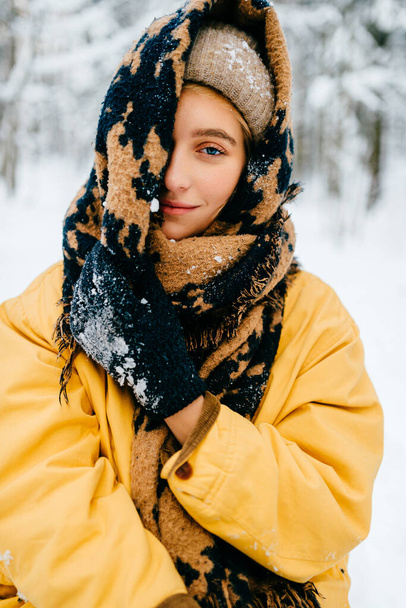 Young stylish hipster girl in yellow jacket covering the head with a warm scarf and posing in the forest - Фото, изображение