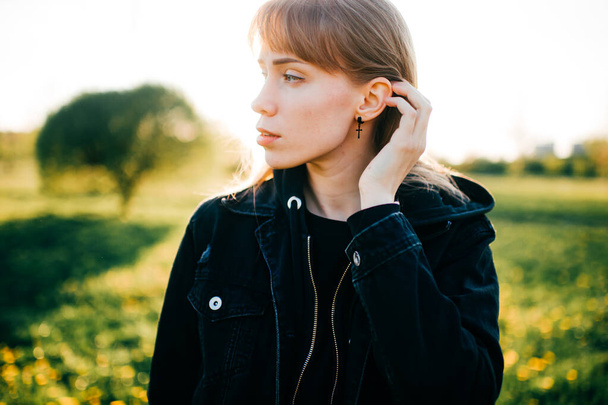 Beautiful young woman with short fair hair and blue eyes in black jacket goes for a walk to the summer park in sunny weather. - Foto, immagini