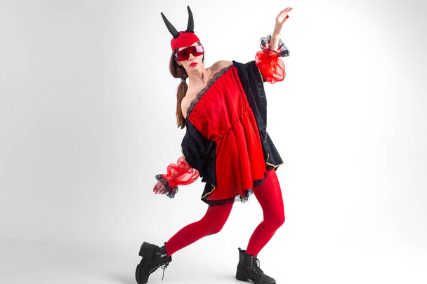 Strange sexy devil woman on red stockings, glasses and devil horns posing in studio. - Photo, Image