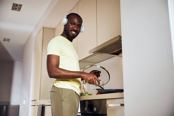 Joyful cook frying his meal with headphones on - Photo, Image