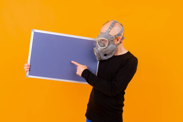 Funny strange man in respirator posing with a board  over orange background - Zdjęcie, obraz
