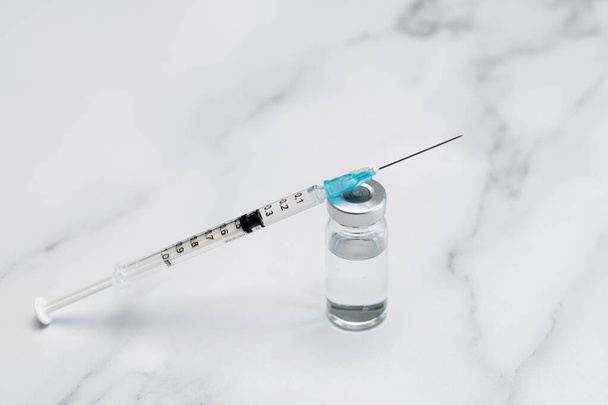 Hypodermiesspritze und unverschlossene Nadel, die auf einem impfstofffertigen Fläschchen ruht - Foto, Bild