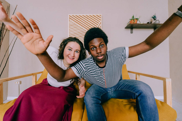Wide angle portrait of interracial couple make faces, laughing and fooling like children. Happy excited dark skinned young man with white girl expressing funny eccentric emotions. Gestures and grimace - Zdjęcie, obraz