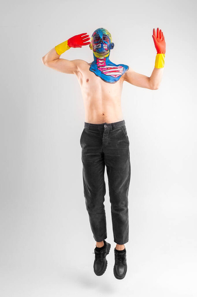 A strange man with makeup on his head and shoulder in red-yellow gloves, black pants and boots, no T-shirt jumps - 写真・画像