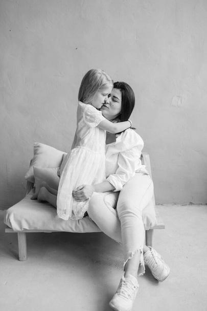 Mother and daughter indoor lifestyle black white portrait. Mom with child have fun in studio. Happiness of motherhood. Mother hugs with her little daughter. Young emotional girl  embraces her mom - Photo, image