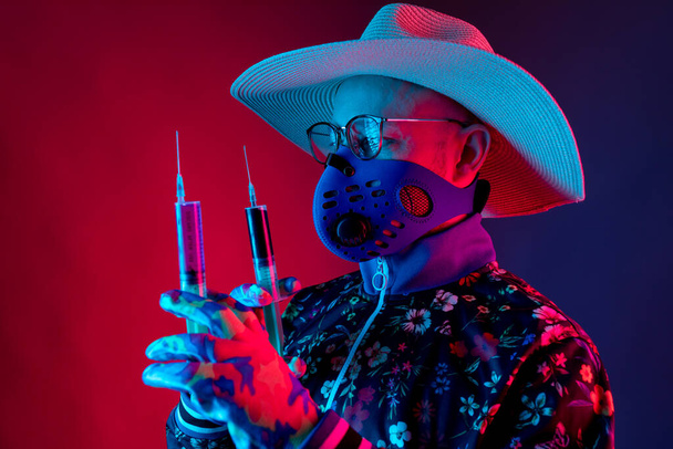 Stylish man wearing medical respirator mas, glasses, hat and gloves and holding two syringes with coronavirus covid 19  blood test. Concept of mad doctor, inventor of corona virus - Фото, зображення