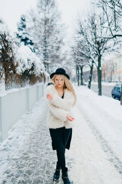 Stylish beautiful blonde girl in coat and hat posing near fence in the street - Fotografie, Obrázek