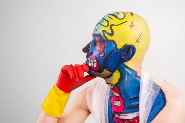 Strange man with makeup on his head and shoulder in white t-shirt, red and yellow gloves, red gesticulates - 写真・画像