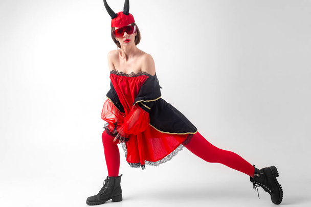 Странная сексуальная дьяволица в красных чулках, очках и дьявольских рогах позирует в студии. - Фото, изображение
