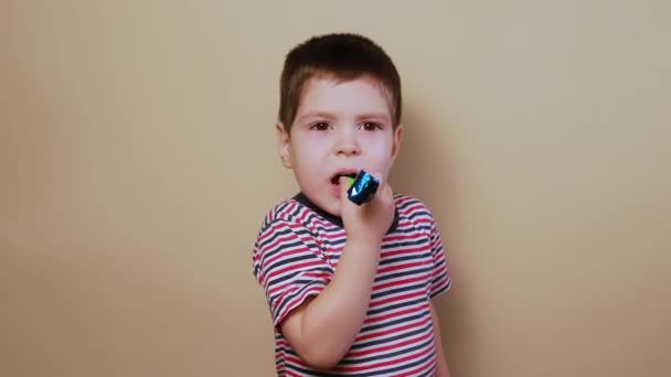 Un bambino piccolo di 3-4 anni suona su un toot di flauto e ride su uno sfondo chiaro beige. Un ragazzo allegro festeggia il suo compleanno, soffiando in un fischio a forma di lingua flauto, gioia per i bambini. Negozio di giocattoli per - Filmati, video