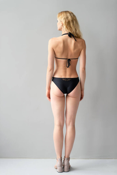 Attractive young blonde model in black swimsut posing in studio - Photo, Image