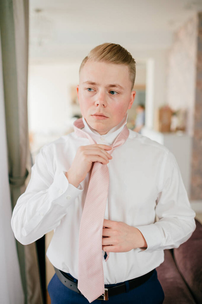 Young groom getting ready. Fiance morning at home. Groom fixing his tie. - Foto, Imagen